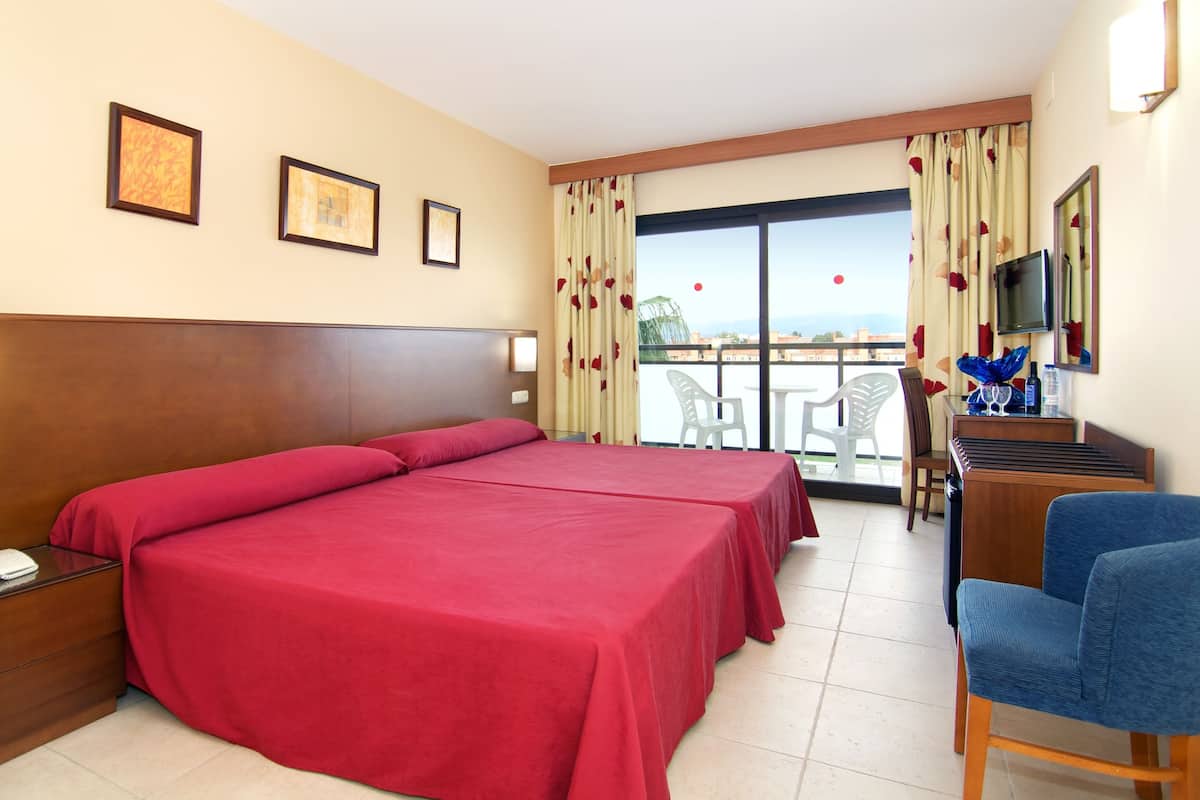 A hotel room with a large bed, a desk with a chair, a telephone, and a television. There are curtains and a window with a view.