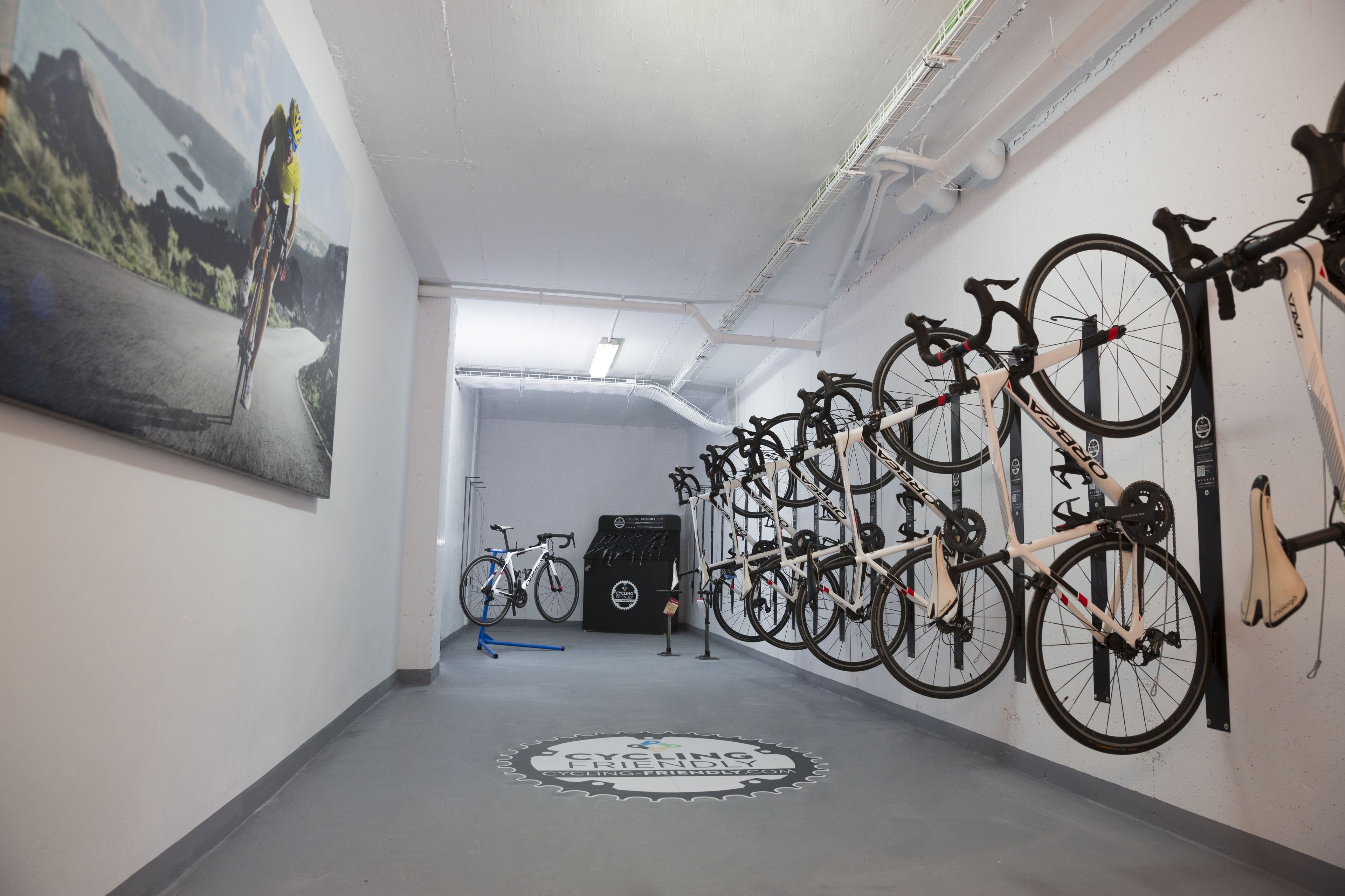 Un couloir où des vélos sont fixés au mur, un tableau sur le côté gauche et un logo au sol.