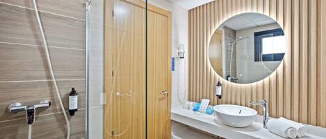 A modern bathroom with a glass shower enclosure, a wooden vanity with a round mirror, and a white sink.