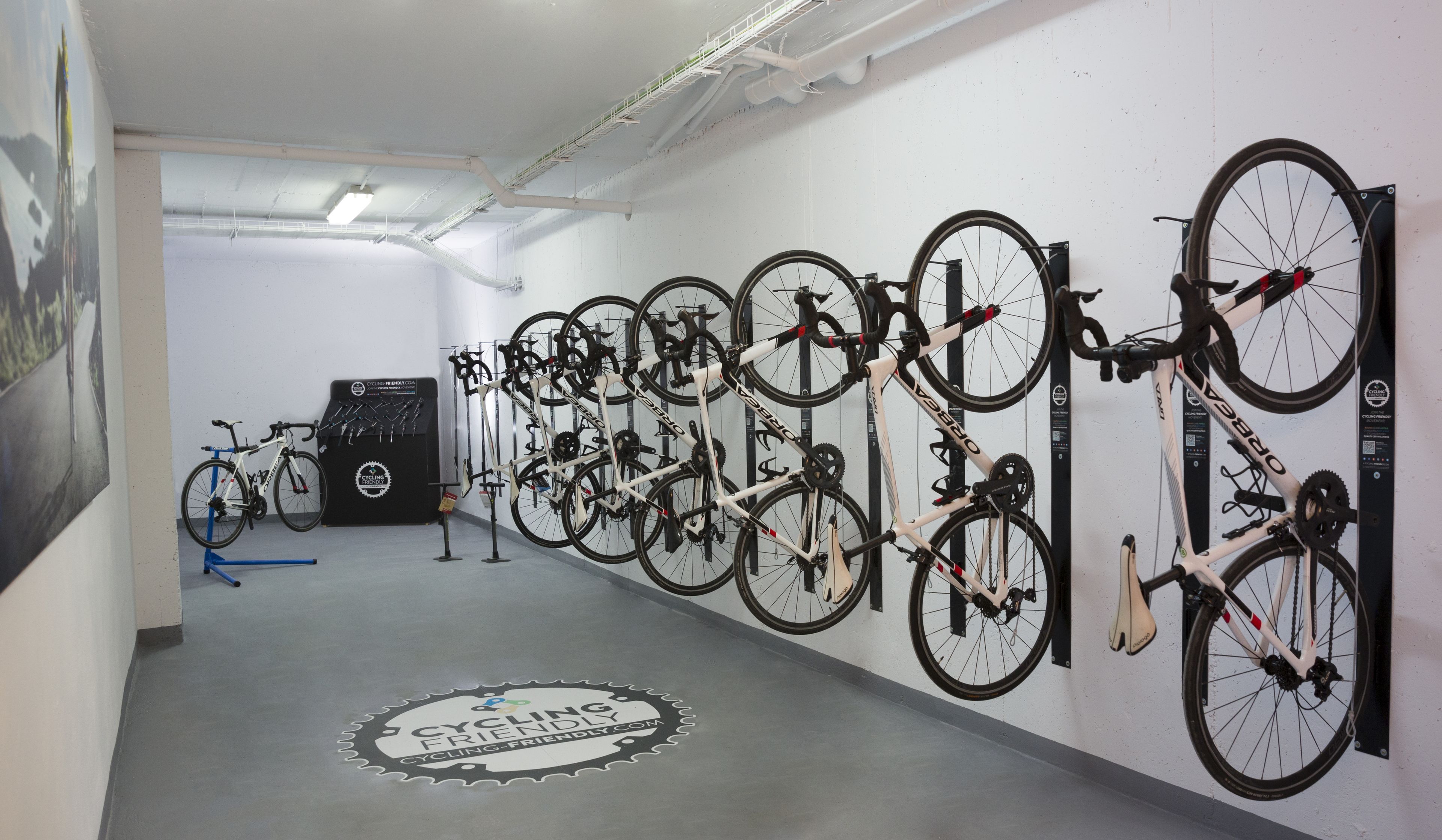 Eine Fahrradwerkstatt mit mehreren an Wänden befestigten Fahrrädern, einem Logo auf dem Boden und einer Decke mit freiliegenden Rohren.