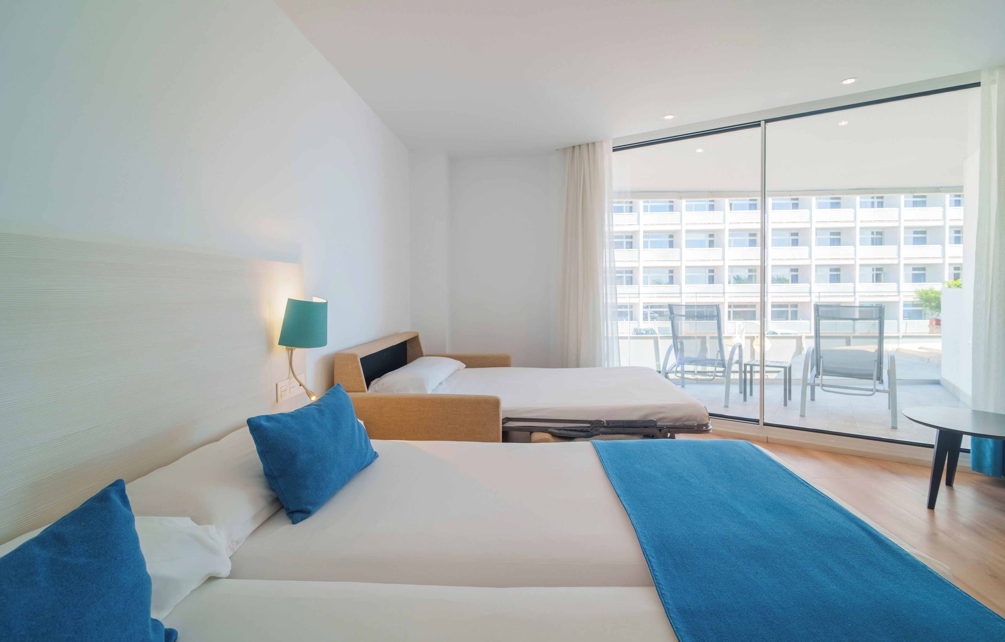 Une chambre d’hôtel avec deux lits, un bureau et une grande fenêtre donnant sur un immeuble.
