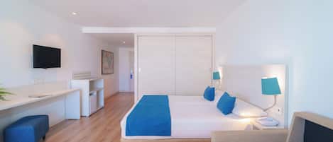 Quarto de hotel moderno com cama, mesa de cabeceira, abajur e escrivaninha com cadeira.