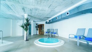 Una piscina interior moderna con diseño circular, rodeada de sillones de descanso y plantas en macetas.