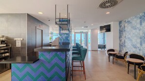 Un área de bar moderna con una barra de diseño chevron, taburetes y una zona de estar con sillas de mimbre.