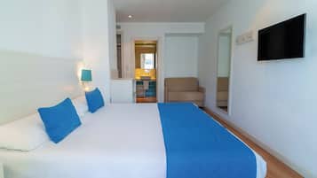 A hotel room with a large bed, a TV mounted on the wall, a chair, and a small kitchenette in the background.