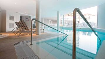 An indoor swimming pool with clear water, a metal safety railing, and lounge chairs.