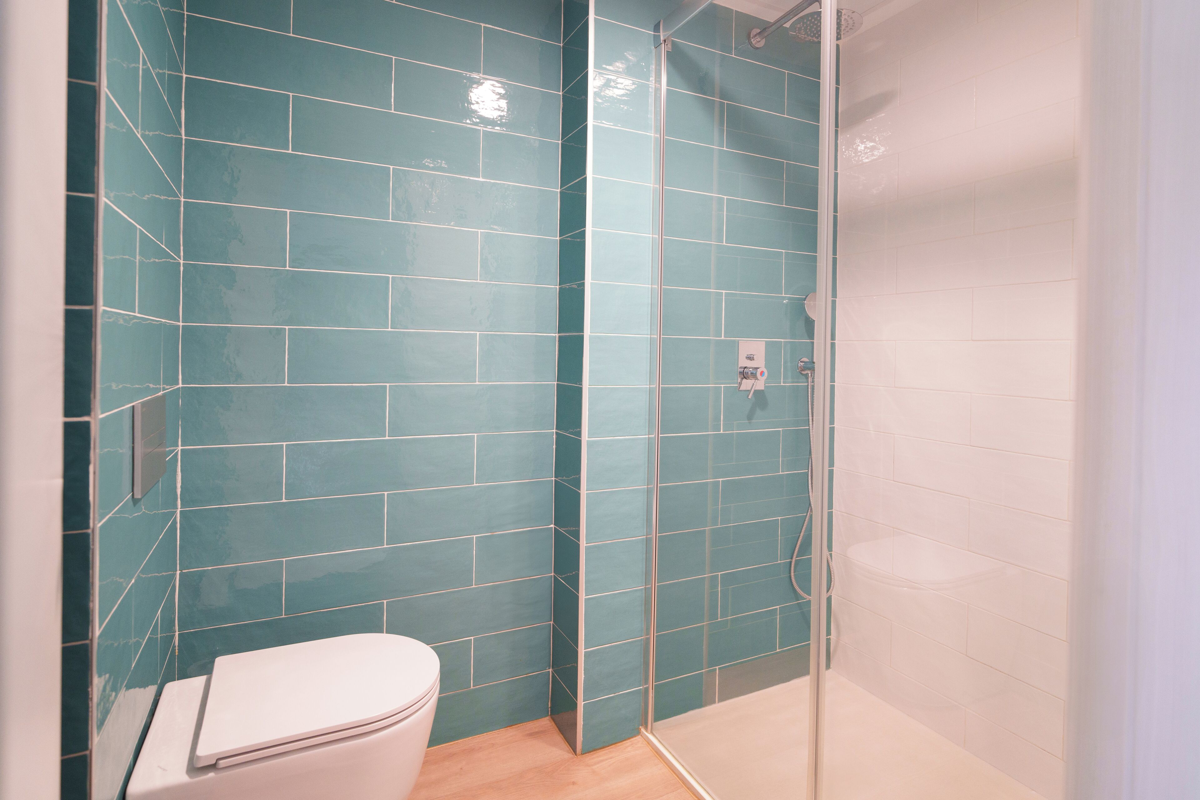 Un bagno con piastrelle color acquamarina, un water bianco e uno spazio doccia in vetro.