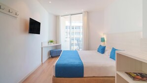 Una habitación de hotel moderna con una cama grande, un escritorio pequeño, un televisor montado en la pared y una ventana con vistas a edificios.