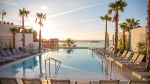 Zona de piscina con tumbonas y palmeras, con vistas al mar.