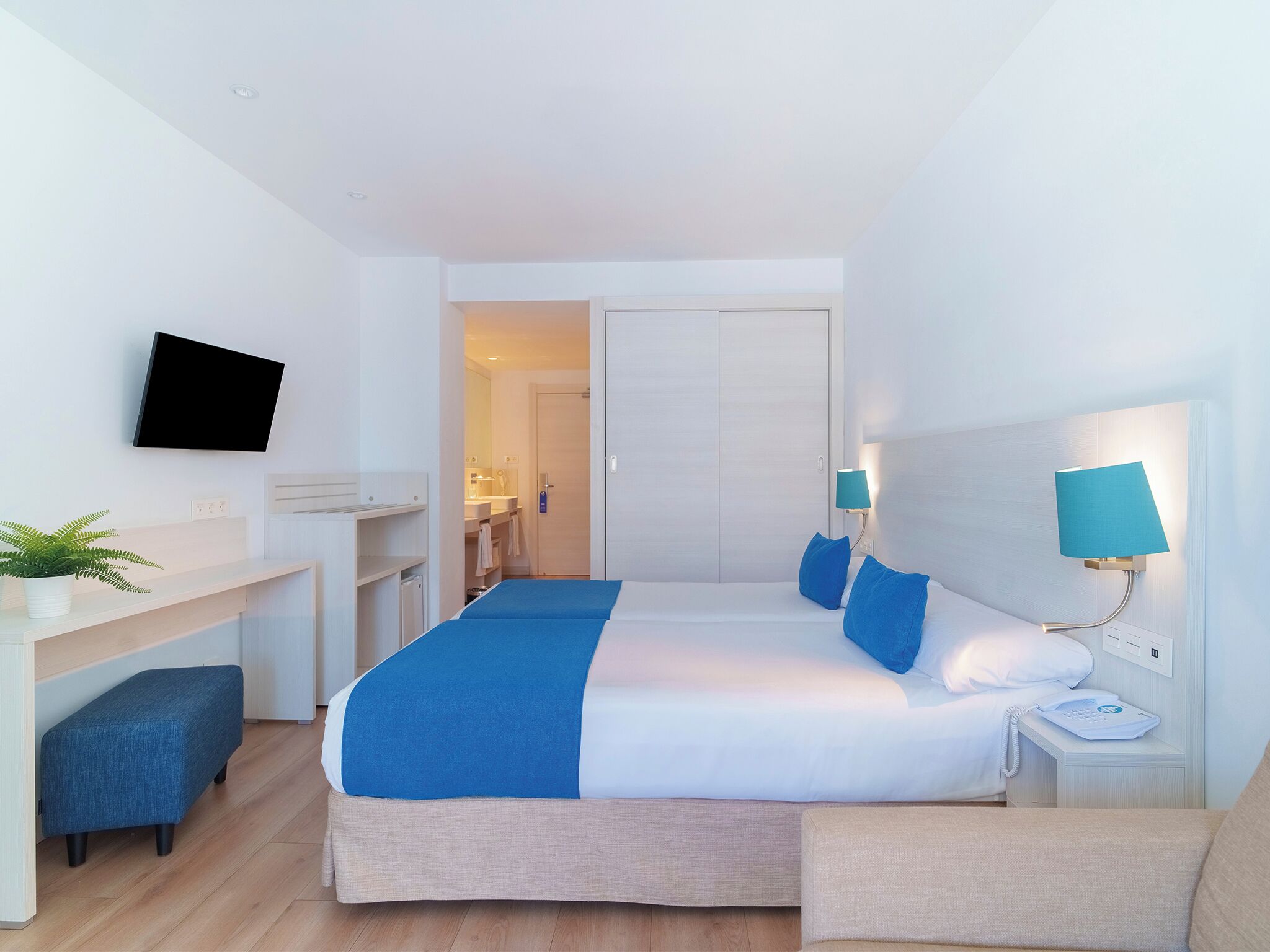 Een moderne hotelkamer met een bed, nachtkastjes, een bureau, een televisie, en een zichtbare badkamer door een geopende deur.