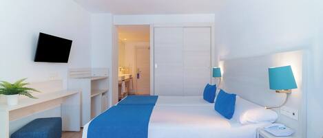 A modern hotel room with a bed, bedside tables, a desk, a TV, and a bathroom visible through an open door.