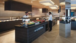 Een moderne buffetopstelling met koks die eten bereiden, met een centraal eiland met diverse gerechten en een lange toonbank met etalages.