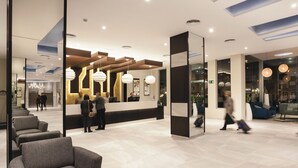 Een moderne hotel lobby met een receptiebalie, zithoek en grote ramen.