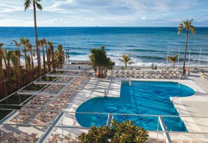 Zona de piscina con sillones de descanso y palmeras, con vista al océano.