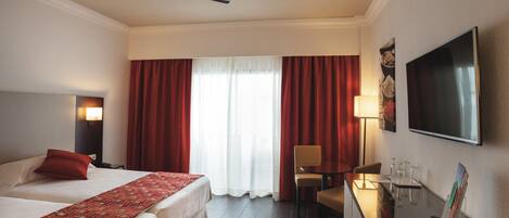 Habitación de hotel con dos camas, un escritorio con silla, televisión y ventilador de techo.