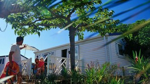 A mobile home with a fenced deck and a tree in the foreground.