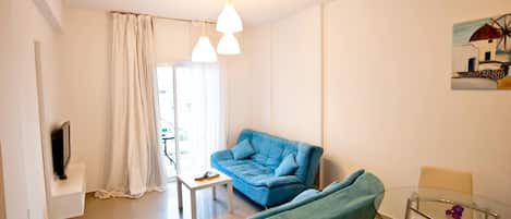 Un salon moderne avec un canapé bleu, une table basse en verre et un téléviseur posé sur un meuble blanc.