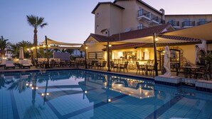 A hotel pool area with a tiled pool, outdoor seating, and a building with balconies. - Anais Bay Hotel (Paralimni)