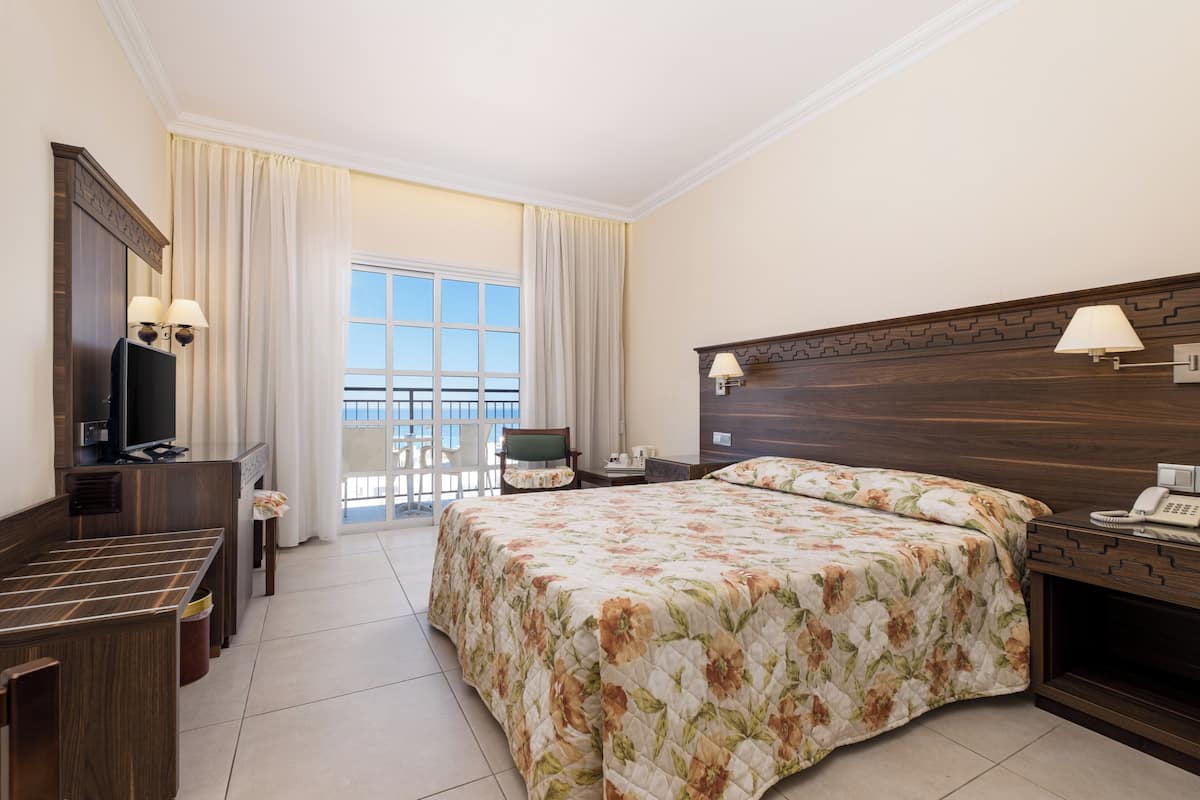 Una habitación de hotel con cama, escritorio, televisor, silla y ventana con cortinas.