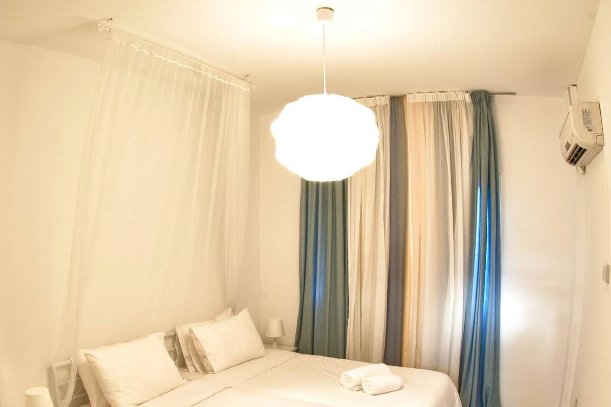 Habitación de hotel con una cama grande, dos mesitas de noche, una silla y una lámpara en el techo.
