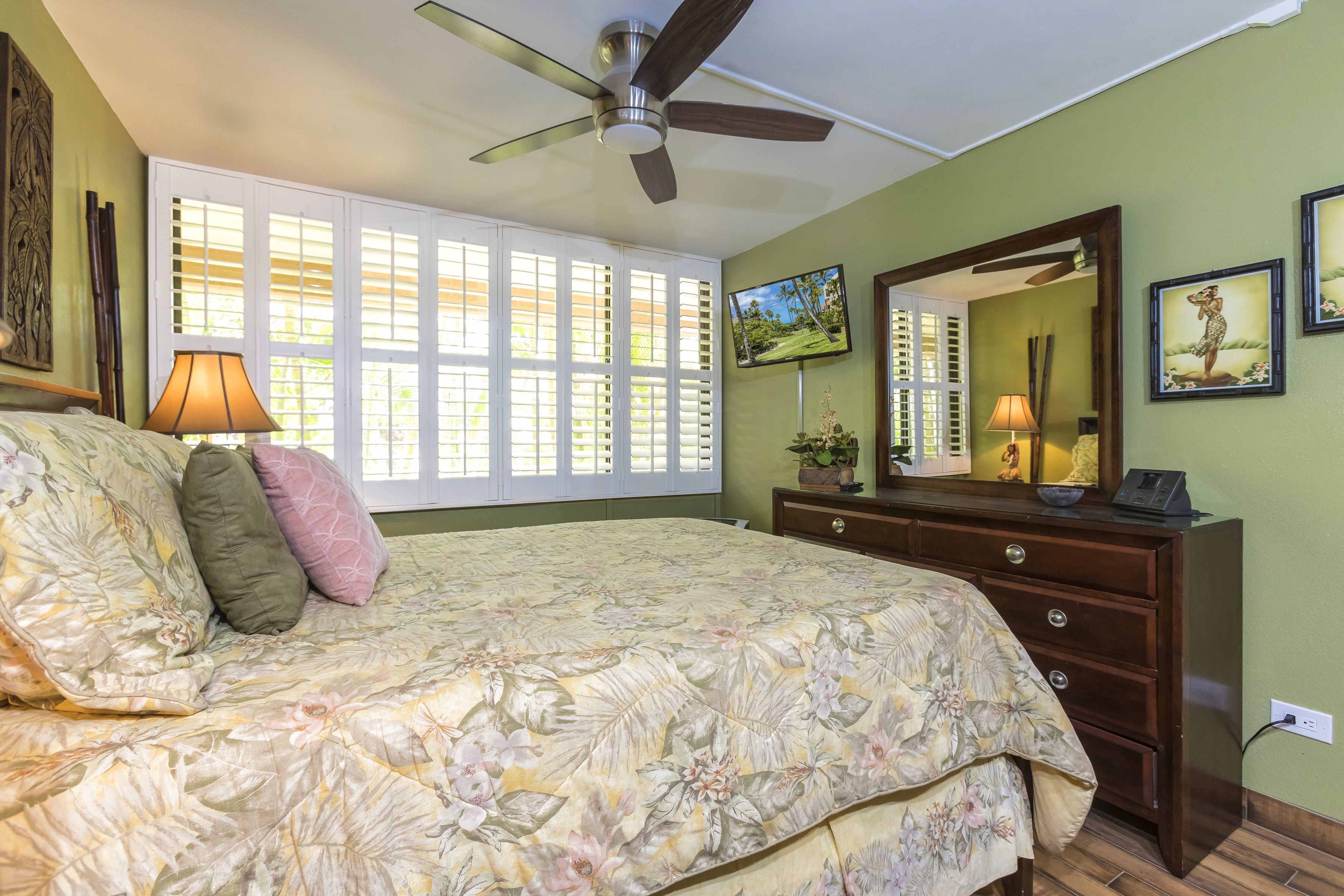 Un dormitorio con cama, cómoda, ventilador de techo y ventana con contraventanas.