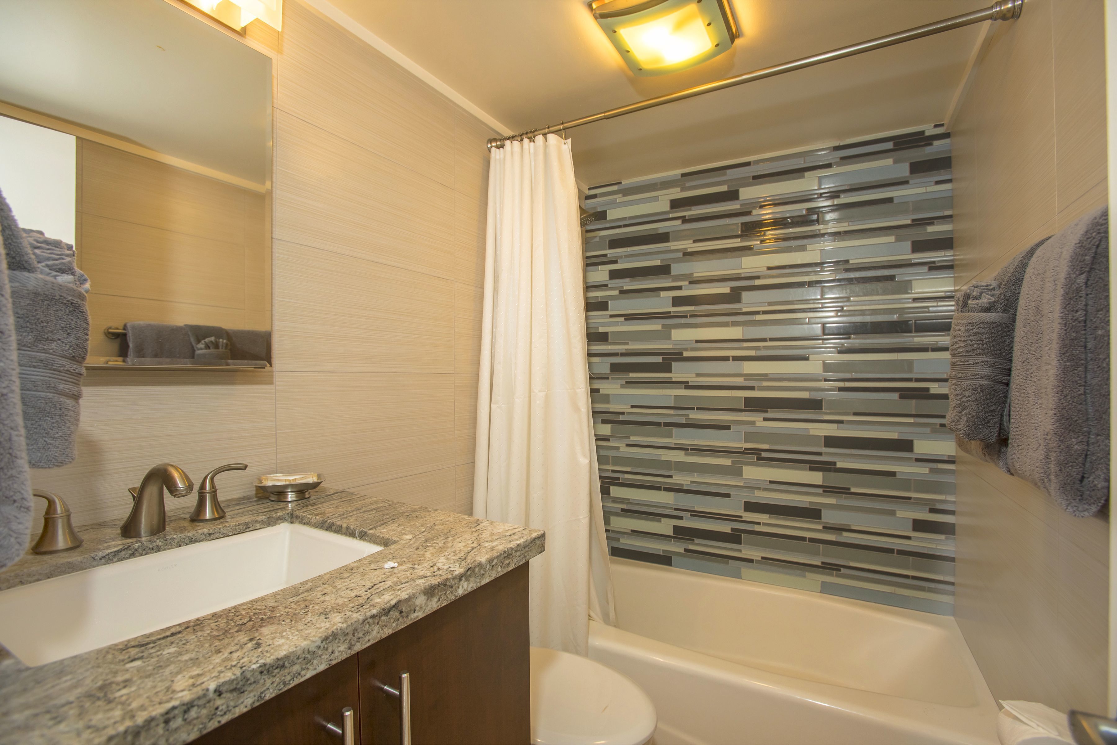 A modern bathroom with a granite countertop sink, a toilet, and a bathtub with a glass mosaic shower curtain.