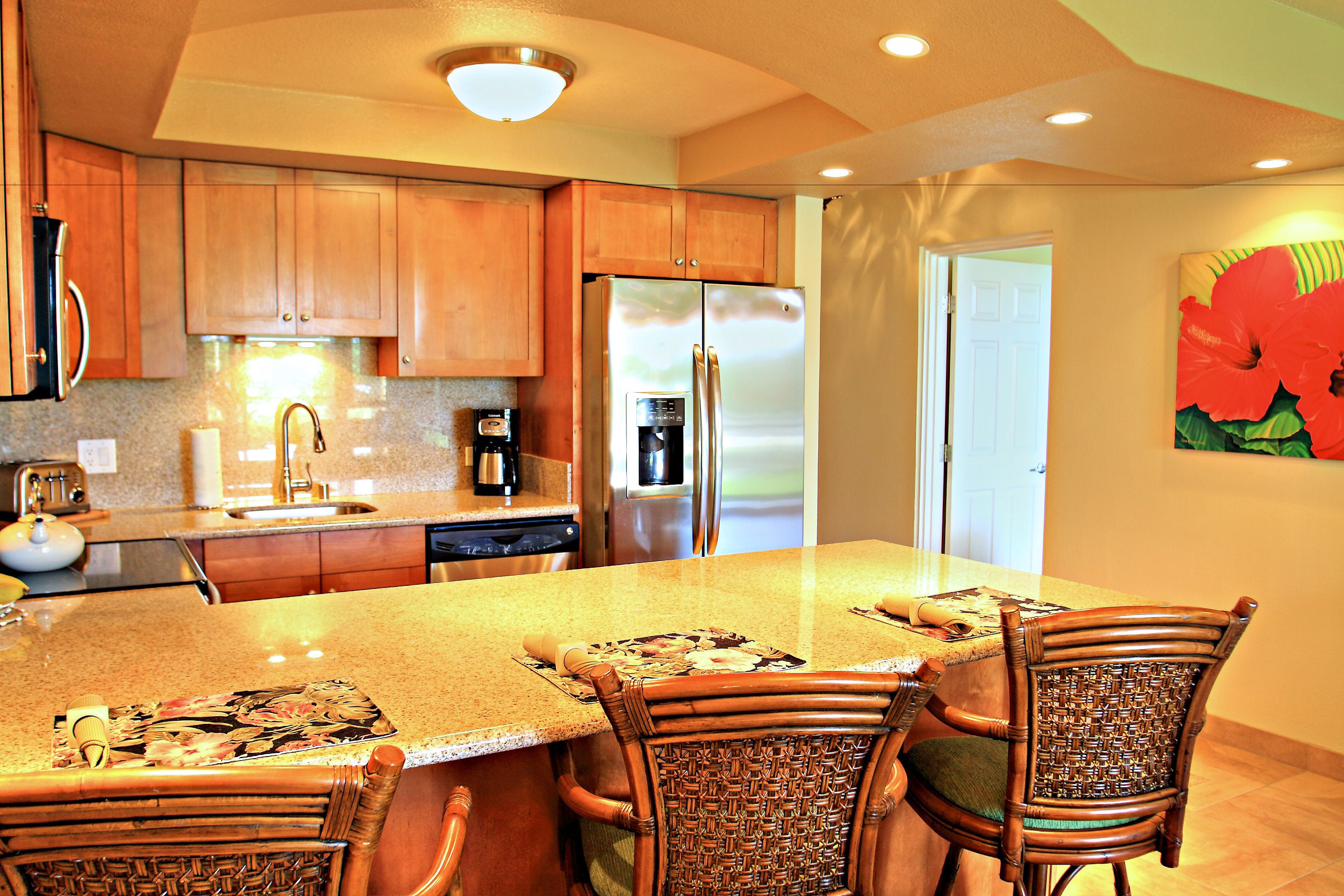 A kitchen with wooden cabinets, a stainless steel refrigerator, and a dining area with wicker chairs.