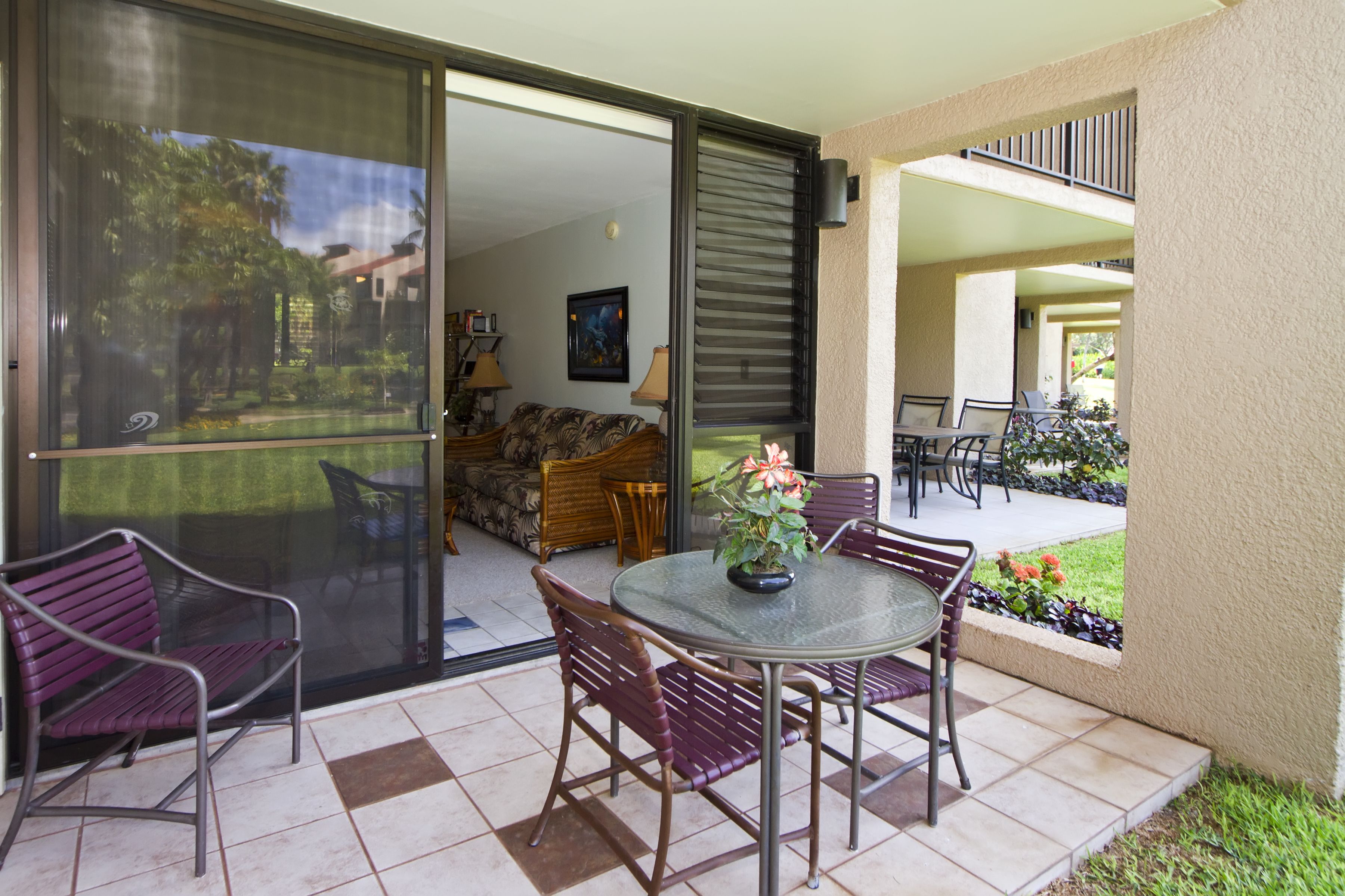 A patio with a glass door leading to a living area, a round table with chairs, and a potted plant.