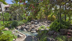 Un jardín ajardinado con una pequeña cascada, rocas grandes y diversas plantas.