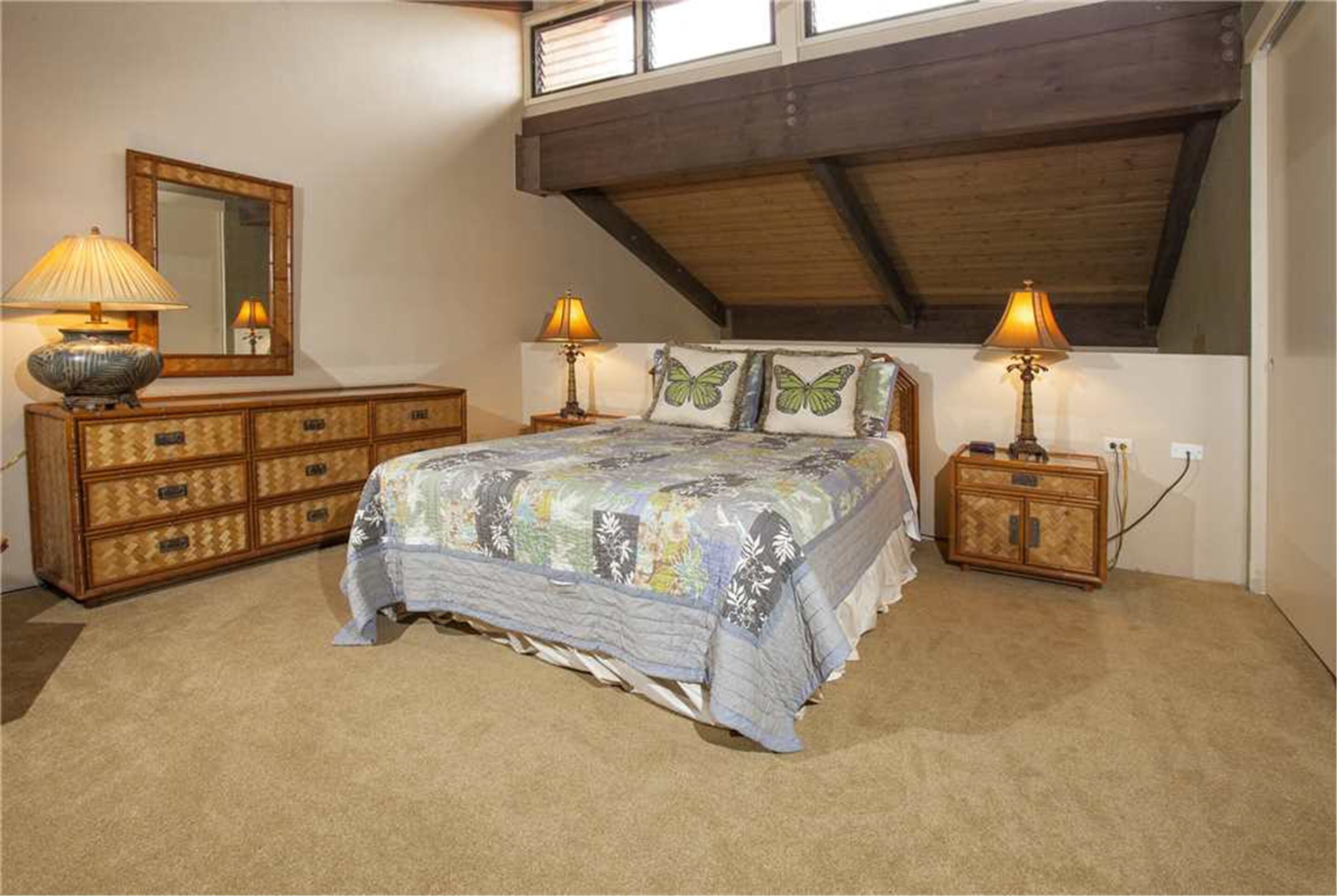 Une chambre à coucher comprenant un lit, deux tables de chevet, une commode, un miroir et un plafond en pente.