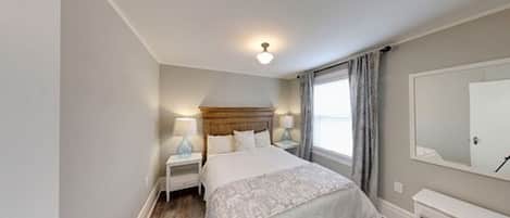 A bedroom with a bed, nightstands, a mirror, and a window with curtains.