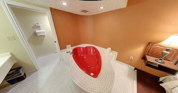 Un baño con una bañera con forma de corazón, un lavamanos blanco y un tocador con espejo.