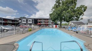 Una piscina con área vallada, sillas de descanso y un edificio con balcones al fondo.