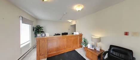 Un espace d’accueil avec un bureau en bois, un fauteuil de bureau noir, une lampe et une plante en pot.