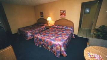 A hotel room with two beds, a wooden headboard, a small table, and a lamp.