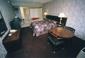 Una habitación de hotel con cama, escritorio, silla, mesa de comedor y dos lámparas.