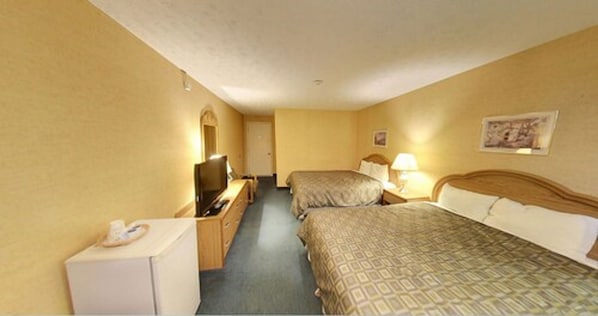 Habitación de hotel con dos camas, televisión, escritorio y un refrigerador pequeño.