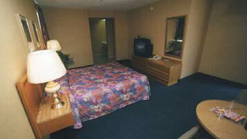 Een hotelkamer met een bed, een dressoir, een televisie, een spiegel en een tafeltje.