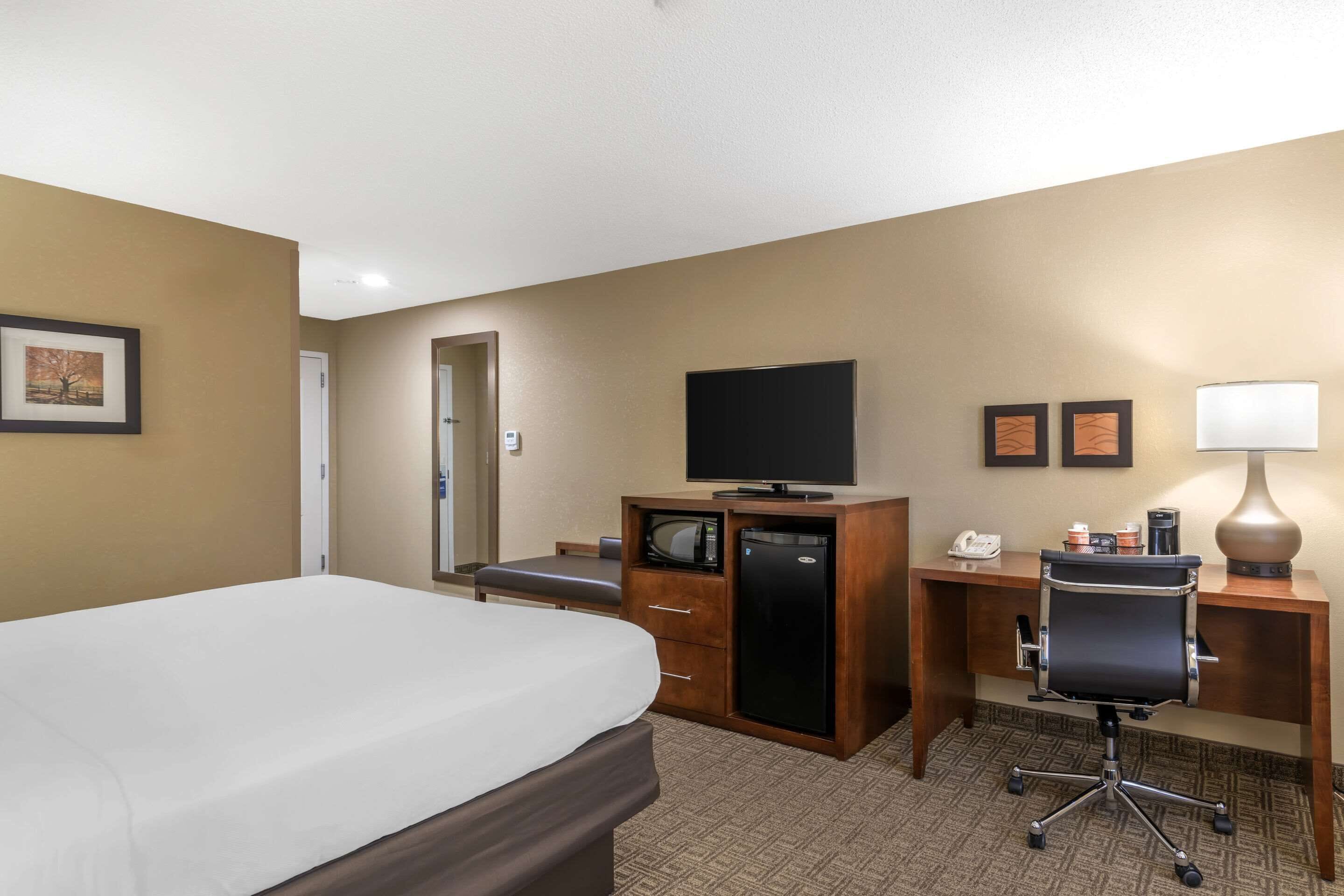 A hotel room with a bed, a desk with a computer, a television, and a desk lamp.