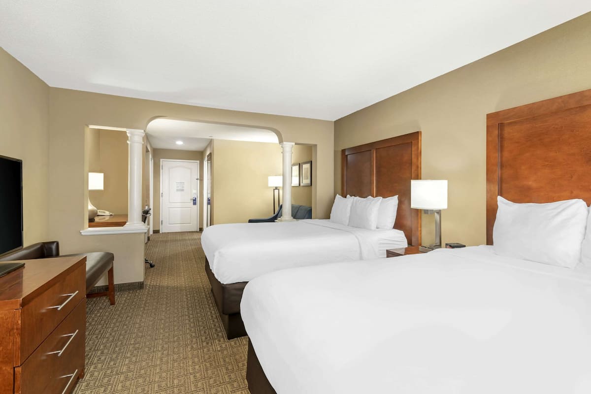 A hotel room with two beds, a desk, a chair, and a television.