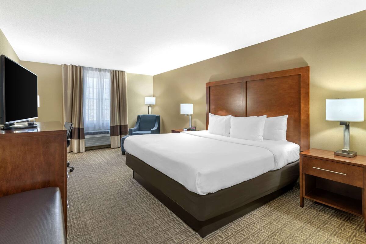 A hotel room with a large bed, a desk with a flat-screen TV, a chair, and two bedside lamps.