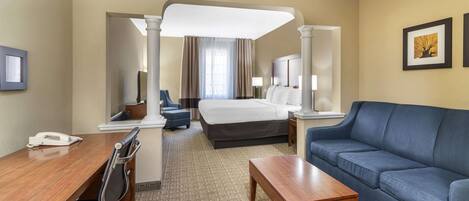 A hotel room with a bed, a blue sofa, a wooden desk, a chair, and a small table.
