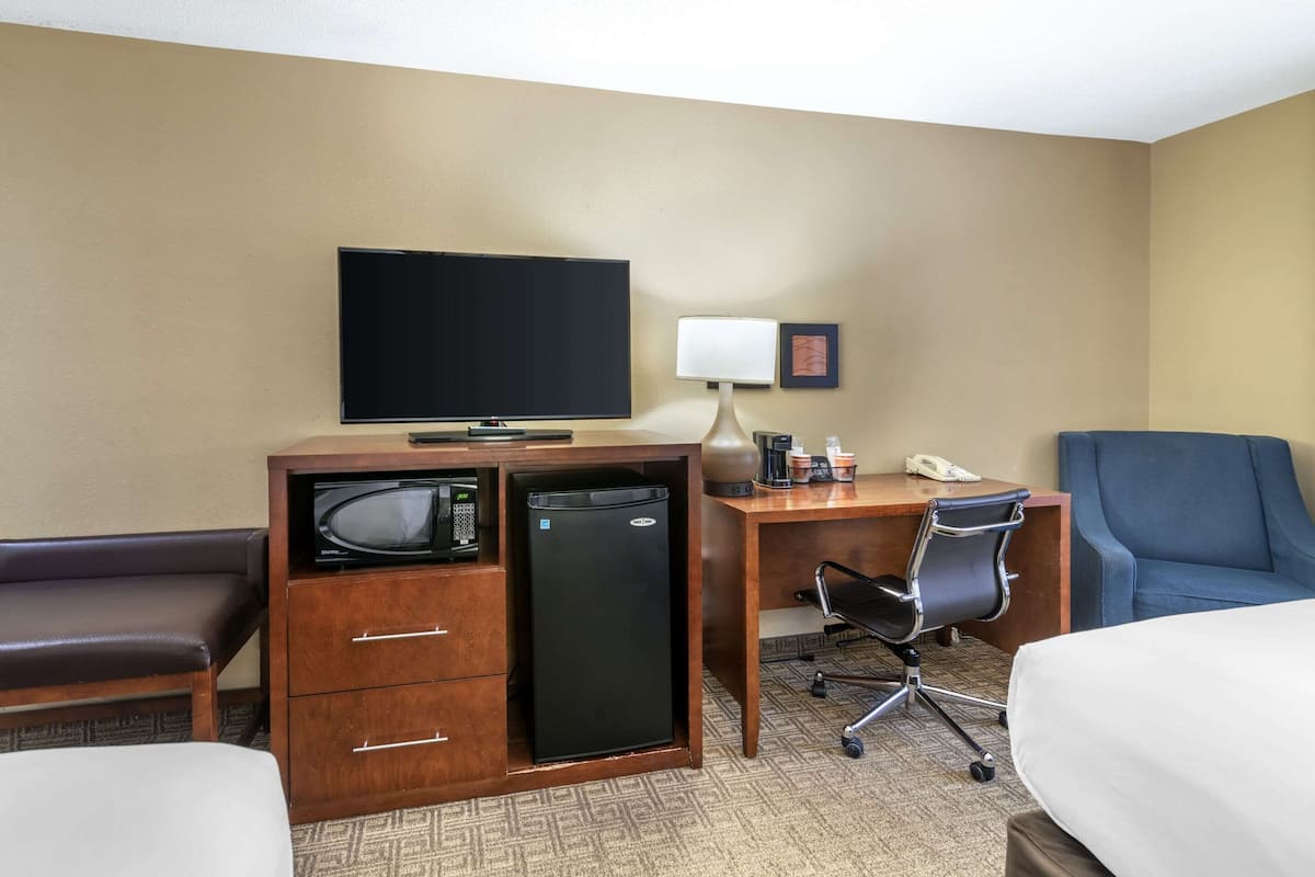 A hotel room with a bed, a desk with a computer, a television, a refrigerator, a microwave, a chair, and a bedside table.