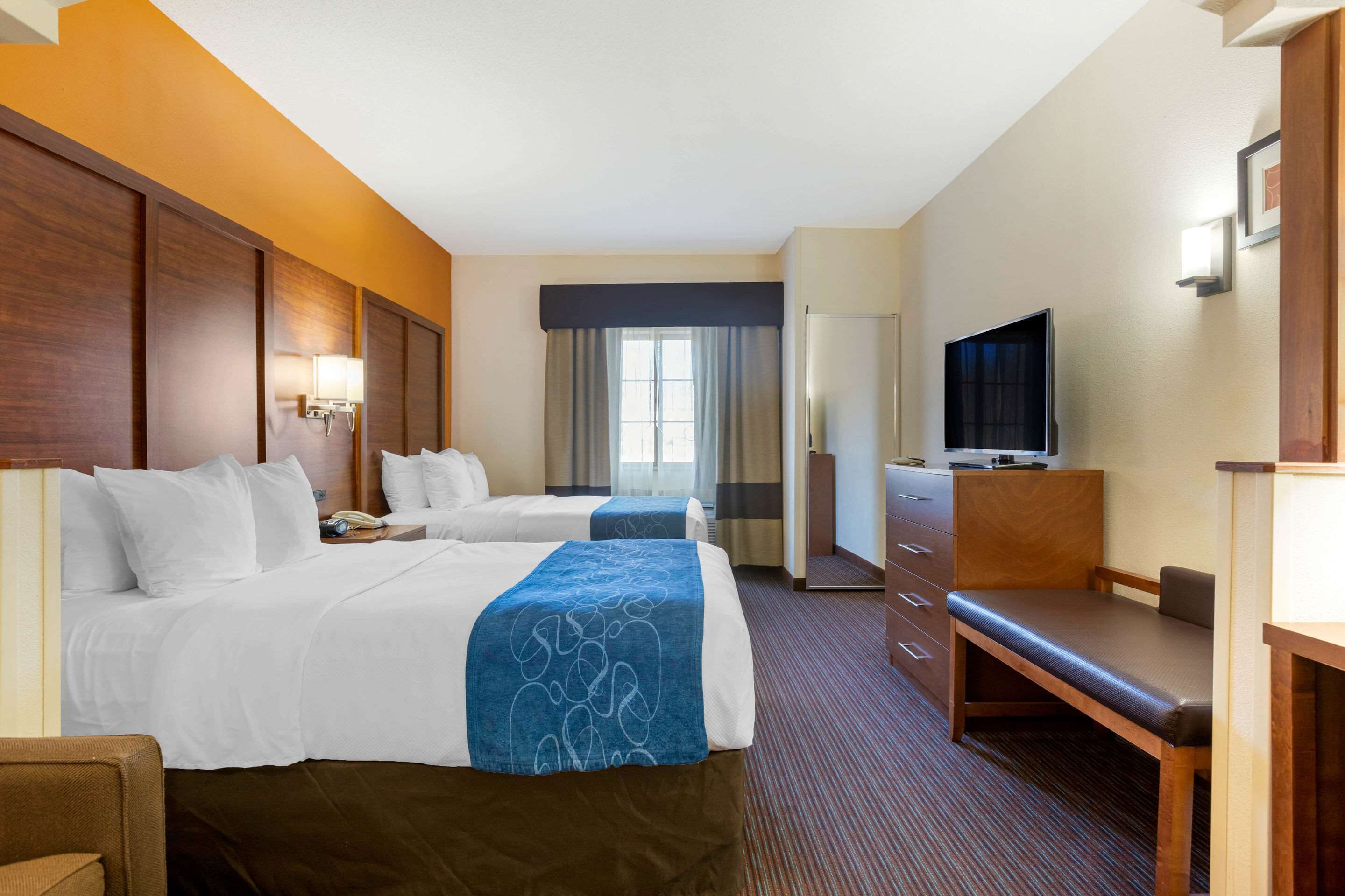 A hotel room with two beds, a desk, a television, and a window with curtains.