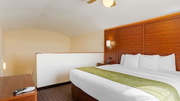 Hotelkamer met een bed, bureau, nachtkastje, wandlamp en plafondventilator.
