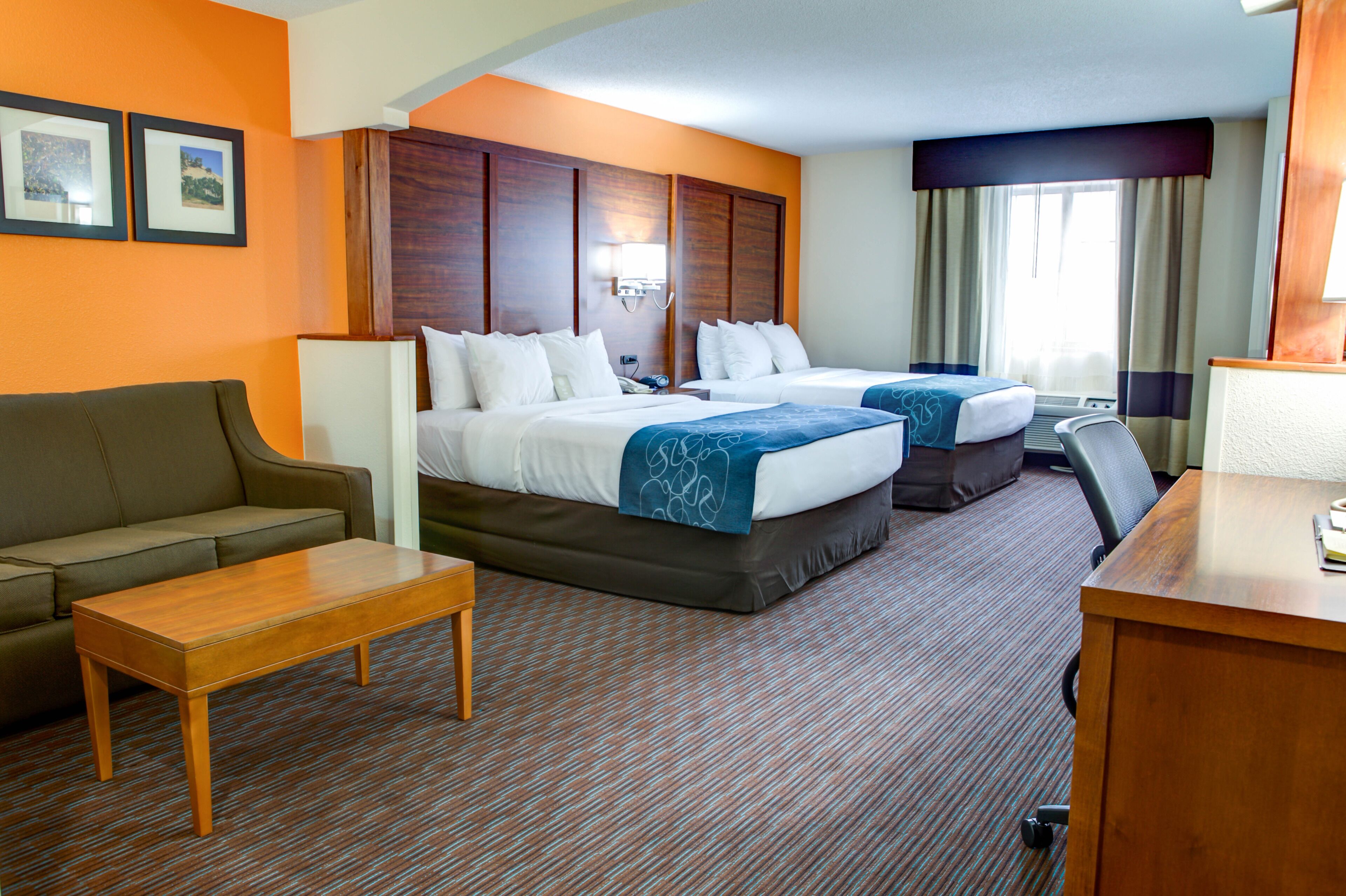 Une chambre d’hôtel avec deux lits, un canapé, un bureau et un sol recouvert de moquette.