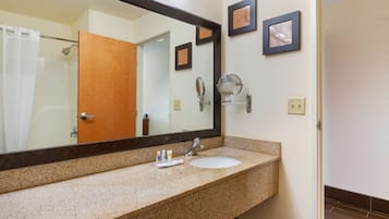 A bathroom with a granite countertop, a sink, a large mirror, and a door leading to a shower.