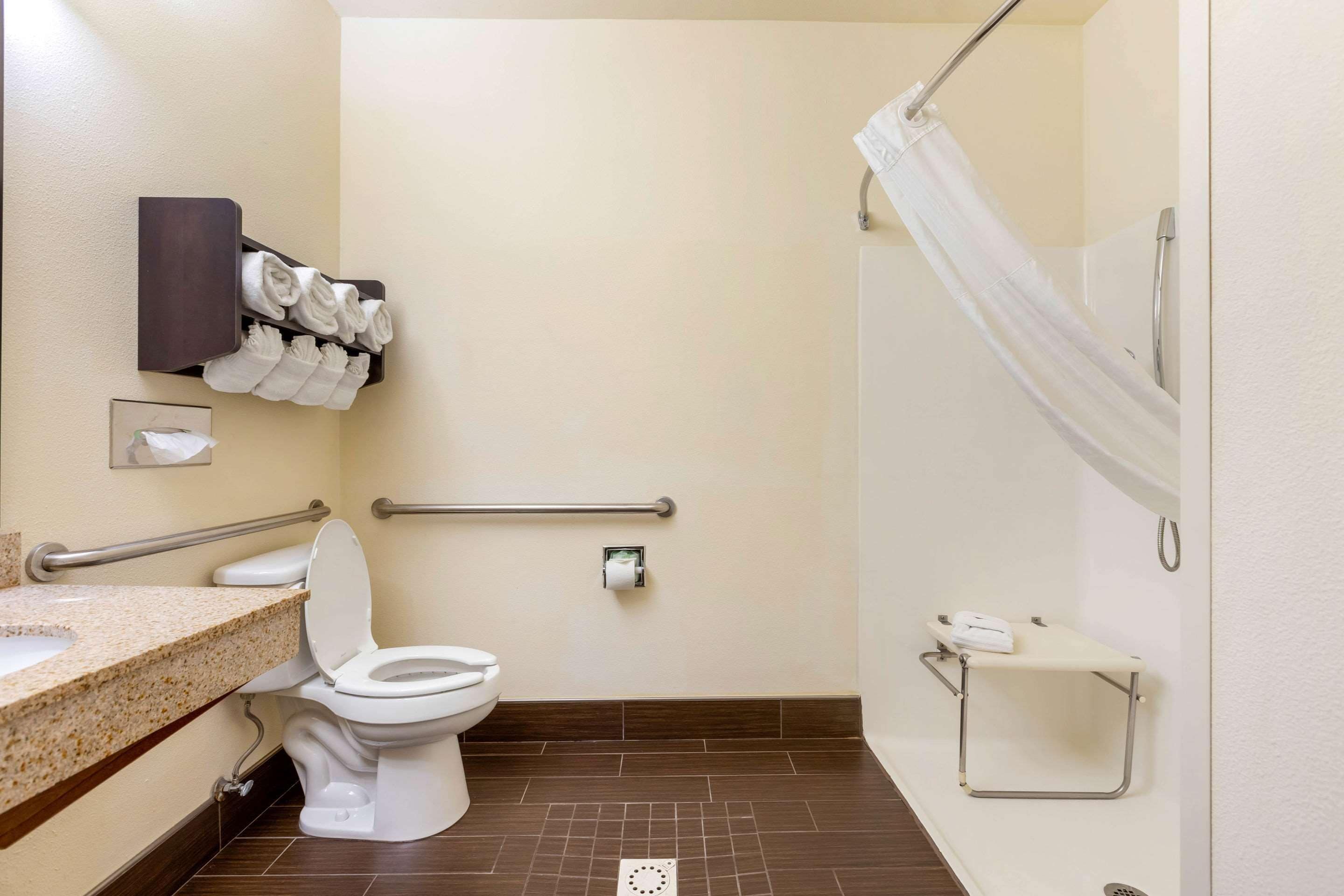 A bathroom with a toilet, a sink, a shower with a curtain, a towel rack, and a handrail.