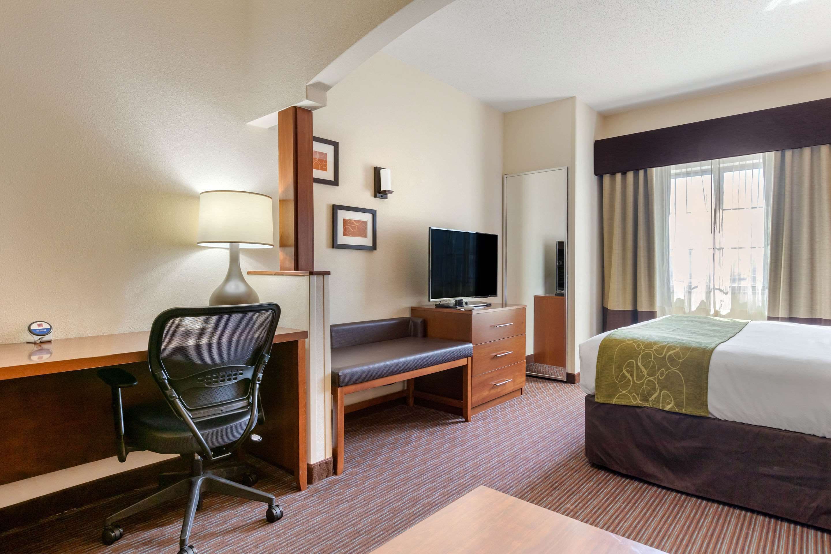 A hotel room with a desk, chair, TV, bed, and a window with curtains.