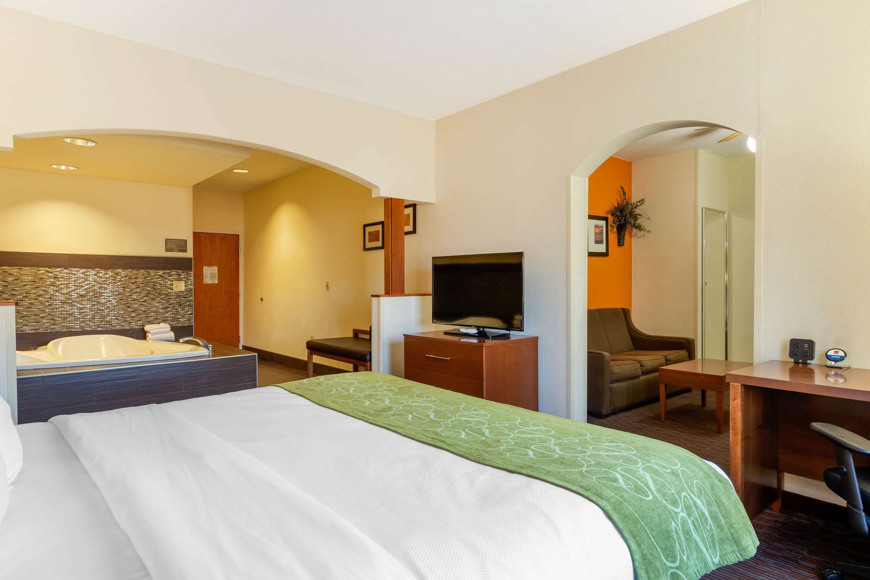 A hotel room with a large bed, a desk, a television, a sofa, and a bathroom with a bathtub and shower.